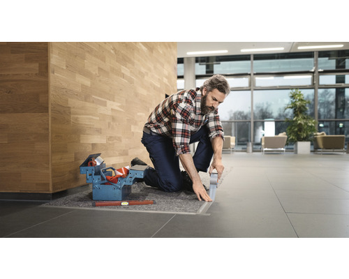 En hantverkare knäböjer och limmar en golvskena i en byggnad.