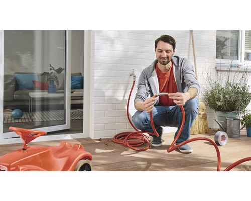 Man ansluter trädgårdsslang på terrassen med leksaksbil för barn.