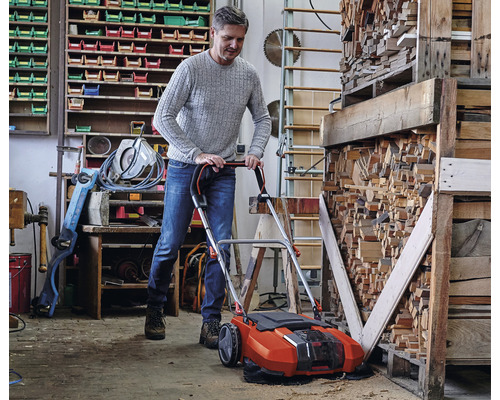 Man använder en batteridriven sopmaskin i en verkstad för att rengöra sågspån.