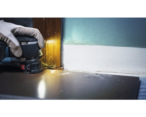 En person använder en multifunktionsslipmaskin för att slipa en trädörrpost.