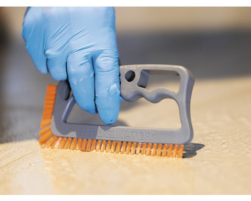 En hand med skyddshandske använder en fogborste för att rengöra kakel.
