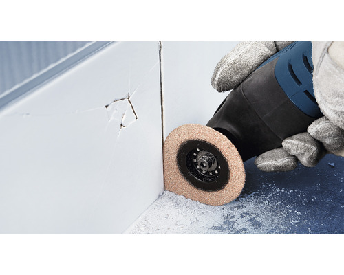 En person använder ett multifunktionsverktyg för att ta bort skadade kakelfogar.