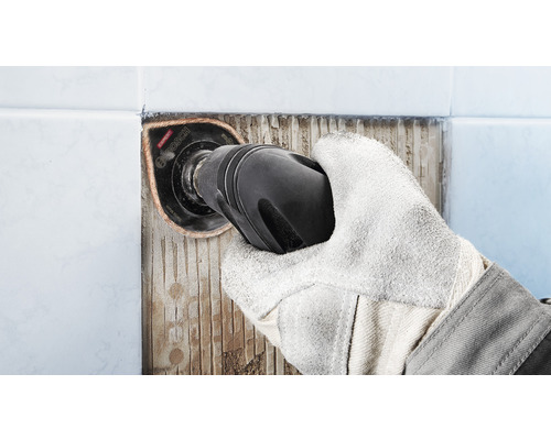 Hand med skyddshandske tar bort kakel med ett multiverktyg