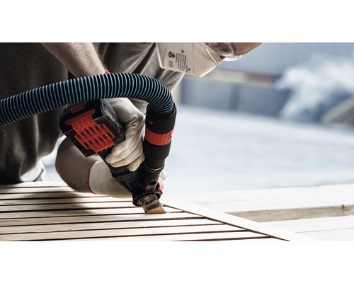 Person slipar trä med ett elverktyg med dammsugaranslutning, skyddsmask och handskar