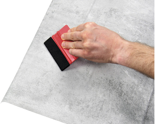 Hand med skrapa applicerar folie med stenmönster