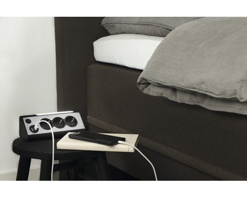 Grenuttag med USB-portar och LED-lampa bredvid en säng på en pall