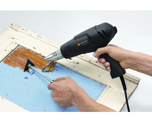 Person tar bort färg från en fönsterkarm med en varmluftspistol och en färgskrapa