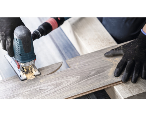 En sticksåg skär en laminatskiva. Skyddshandskar används.