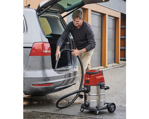 En man använder en våt- och torrdammsugare för att rengöra insidan av en bil.