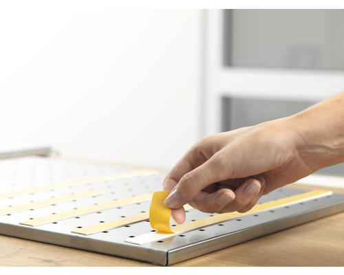 Hand fäster dubbelsidig tejp på en perforerad plåt av metall.