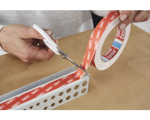 En person skär Tesa dubbelhäftande tejp med en sax för att fästa den i en metallskena.
