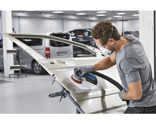 En man slipar en bildörr med en slipmaskin i en verkstad.