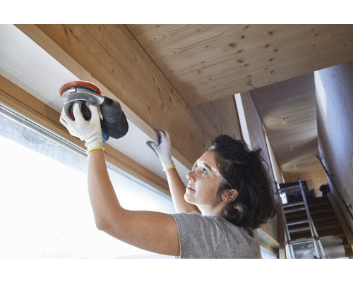 En kvinna slipar en fönsterram av trä med en excenterslip.