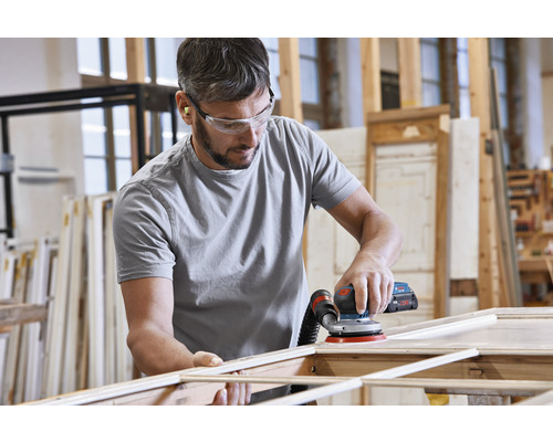 En man slipar trä med en excenterslipmaskin i en verkstad.