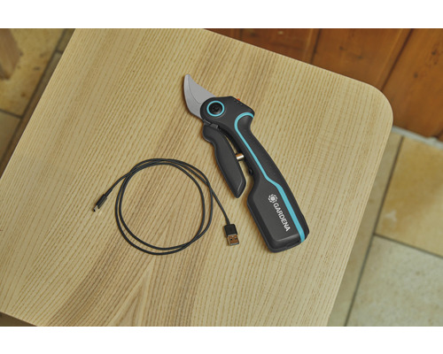 Gardena batteridriven trädgårdssax med USB-laddningskabel på ett träbord