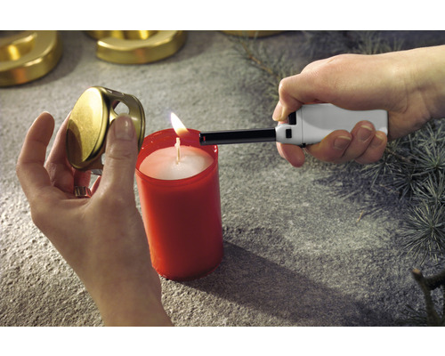 En person tänder ett ljus med en tändare. Ljuslocket hålls i handen.