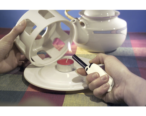 Tända ett värmeljus under en tekokare med en tändare.