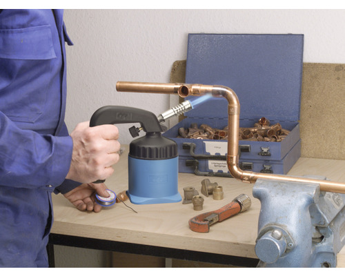 Hantverkare löder kopparrör med en lödbrännare, rörtång och kopparrördelar på en arbetsbänk