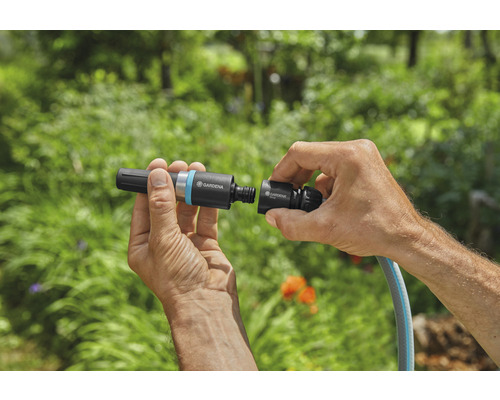 En person ansluter en Gardena slangkoppling till en trädgårdsslang.