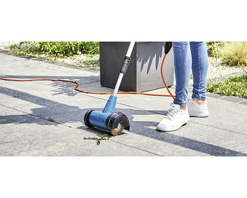 Person använder en elektrisk fogborste på stenläggning i trädgården.