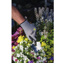 Person med trädgårdshandskar och planteringsspade planterar blommor