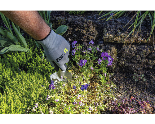 En person med trädgårdshandskar arbetar med en planteringsspade i en rabatt.