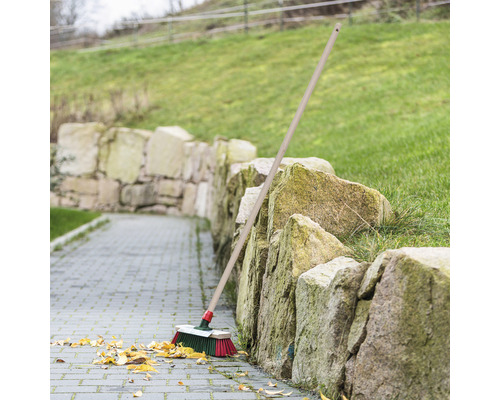 Sopborste med träskaft lutar mot en stenmur på en stenlagd stig med löv