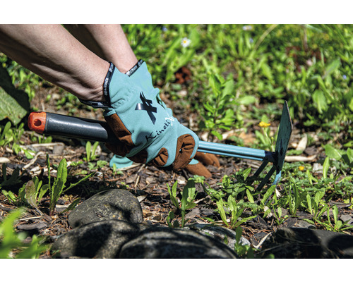 Person tar bort ogräs med en trädgårdshacka och bär trädgårdshandskar.