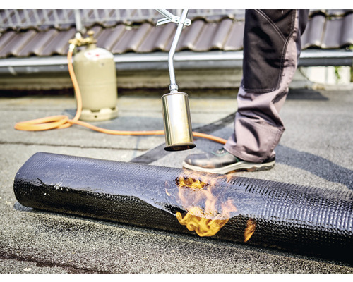 Takläggare svetsar bitumenmembran med en brännare, gasflaska i bakgrunden