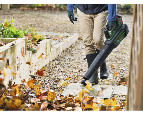 En person använder en batteridriven lövblåsare i trädgården för att ta bort löv.