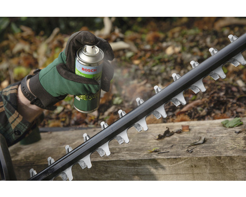En person sprayar bladet på en häcksax med en underhållsspray från Bosch.
