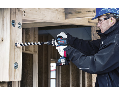 En byggnadsarbetare borrar ett hål i en träbjälke med en sladdlös skruvdragare.