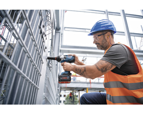 En arbetare använder en sladdlös mutterdragare på en metallkonstruktion.