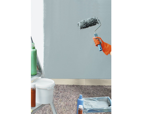 Måla vägg med färgroller, färgburk och täckmaterial på golvet.