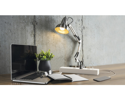 Arbetsplats med skrivbordslampa, laptop och grenuttag på ett skrivbord.