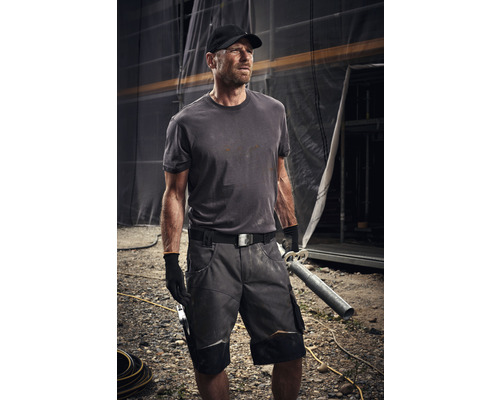 Hantverkare bär arbetskläder med shorts, t-shirt, bälte och handskar på en byggarbetsplats