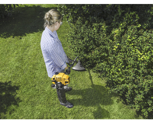 Kvinna arbetar med en gul grästrimmer i trädgården.