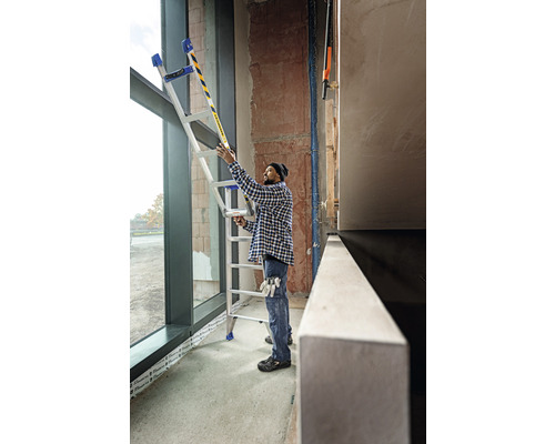 En person använder en multifunktionell stege vid ett fönster på en byggarbetsplats.