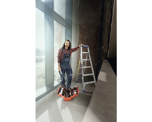 En man står på en verktygslåda med verktyg, bredvid honom en stege.