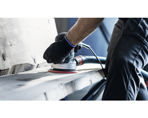 En person slipar trä med en elektrisk excenterslipmaskin.