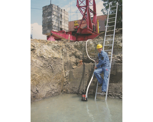 Byggnadsgrop med vatten, dränkbar pump, arbetare på stege och kran i bakgrunden