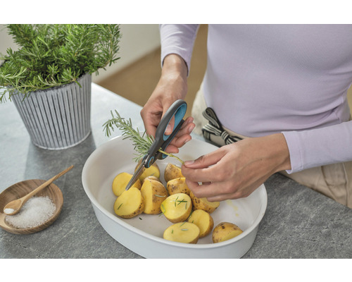 Person klipper rosmarin med en sax över en skål med potatis.