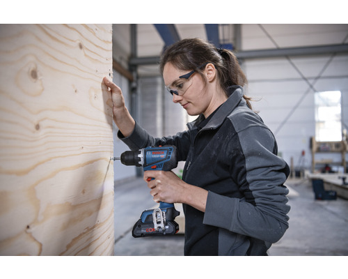 Kvinna skruvar skruv i trä med sladdlös skruvdragare