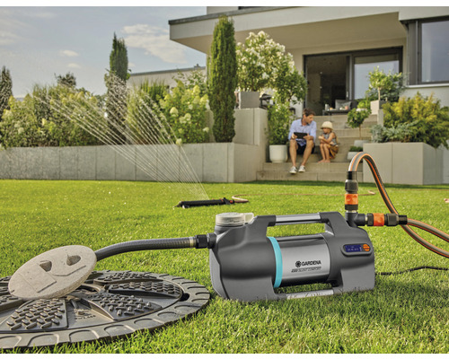 Gardena hydroforpump med tillbehör i trädgården, medan en pappa och ett barn sitter på terrassen