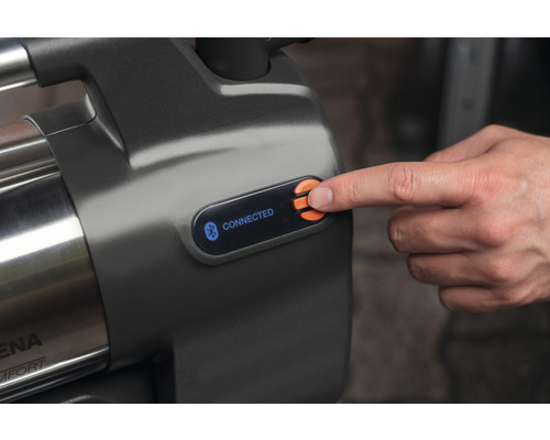 Detaljvy av en trädgårdspump med Bluetooth-funktion och kontrollpanel, där ett finger trycker på en knapp.