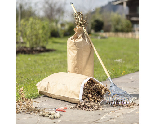 Trädgårdsscen med två papperssäckar fyllda med trädgårdsavfall, en räfsa, en trädgårdssax och trädgårdshandskar.