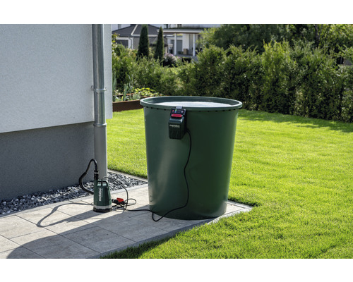 Trädgårdsscen med regnvattentunna, husvägg, stuprör och dränkbar pump med Metabo-logotyp