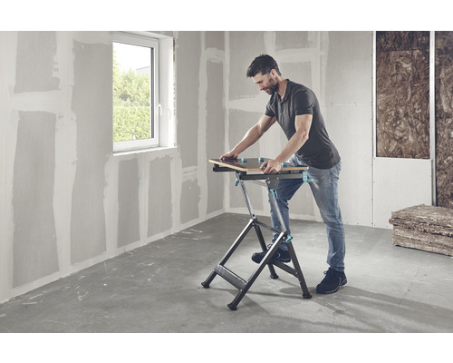 Man arbetar med en arbetsbänk i ett rum med gipsväggar och ett fönster.