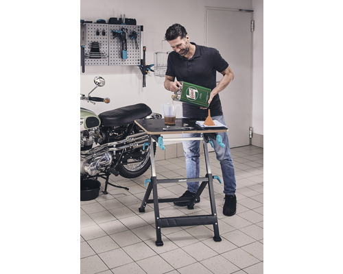 Man häller olja på arbetsbänk i garage, med en motorcykel och verktygsvägg i bakgrunden.