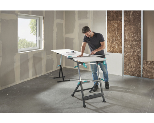 Man skär gipsskivor på ett Wolfcraft arbetsbord i ett oinrett rum.